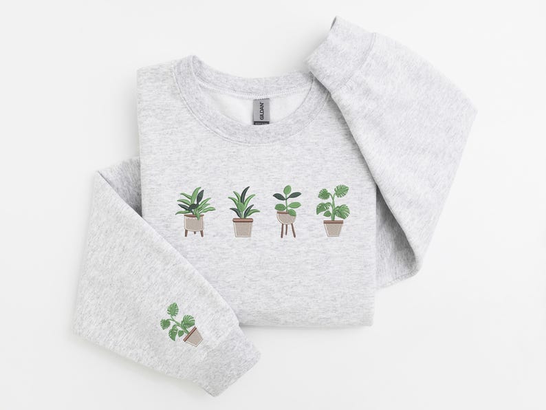 Pode incluir: Uma camisa de moletom cinza com um gr&aacute;fico de cinco plantas em vasos. As plantas s&atilde;o verdes e marrons e est&atilde;o dispostas em uma fileira na frente da camisa de moletom.