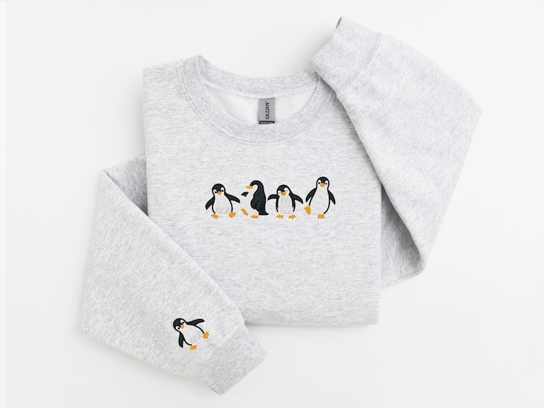 Pu&ograve; includere: Una felpa grigio chiaro con girocollo e maniche lunghe. La parte anteriore della felpa presenta un disegno ricamato di cinque pinguini. Un pinguino &egrave; ricamato sulla manica sinistra.