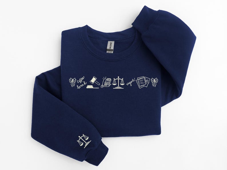 Pode incluir: Camisola azul marinho com desenhos a tra&ccedil;o brancos de s&iacute;mbolos legais e texto. O design inclui um martelo, balan&ccedil;as e documentos. A manga apresenta um &iacute;cone de balan&ccedil;as. O texto inclui "Coffee break" e "Urgent!"