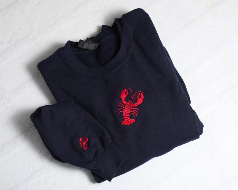 May include: A navy blue sweatshirt with a red embroidered lobster on the front. The sweatshirt has a small red embroidered lobster on the sleeve.