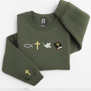 May include: A dark green sweatshirt with embroidered religious symbols, including a fish, a cross, a dove with an olive branch, and a closed book with a cross on the cover.
