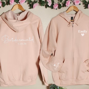 Pu&ograve; includere: Due felpe con cappuccio rosa con cerniera. Una felpa ha "Bridemaid 7.18.20" sul retro. L'altra felpa ha "Emily" e un cuore sul davanti e "7.18.20" sulla manica.