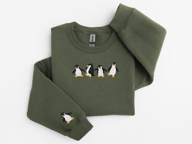 Pu&ograve; includere: Felpa verde oliva con un design ricamato di cinque pinguini. I pinguini sono neri e bianchi con piedi e becchi arancioni. Un pinguino &egrave; ricamato sulla manica sinistra. La felpa &egrave; realizzata in materiale morbido.