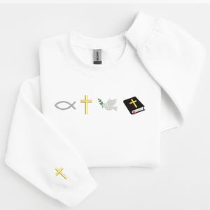 May include: White sweatshirt with a gold cross, a dove, a fish, a green olive branch, and a closed black book with a gold cross on the cover.