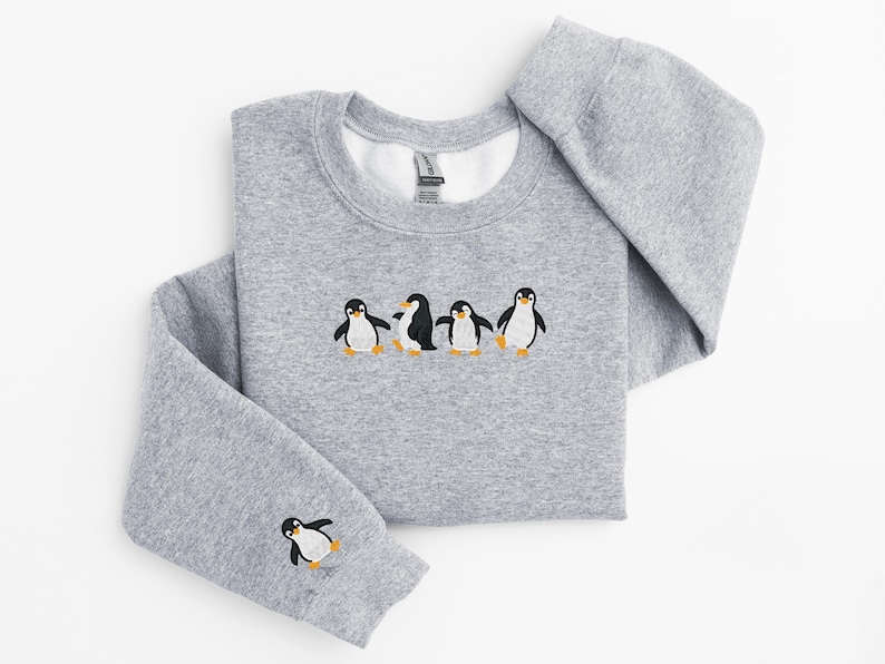 Pu&ograve; includere: Una felpa grigio m&eacute;lange con girocollo e maniche lunghe. La parte anteriore della felpa presenta un disegno ricamato di cinque pinguini. Un pinguino &egrave; ricamato sulla manica sinistra.