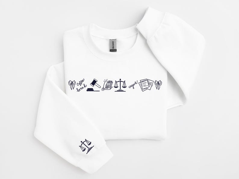 Pode incluir: Camisola branca com gola redonda e mangas compridas. A frente apresenta uma linha de arte de linha preta, incluindo um martelo, balan&ccedil;as e texto que diz "coffee break" e "urgent!". A manga esquerda tem um gr&aacute;fico de balan&ccedil;as.