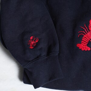 May include: A navy blue sweatshirt with red embroidered lobster designs on the sleeves.