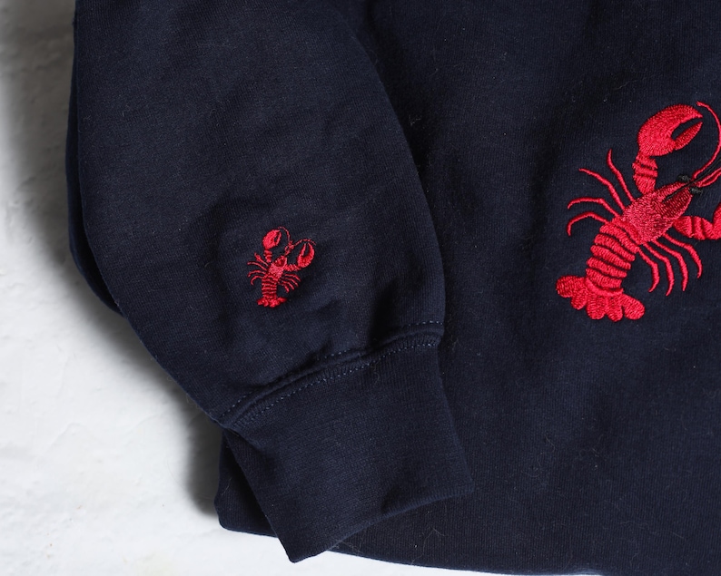 May include: A navy blue sweatshirt with red embroidered lobster designs on the sleeves.