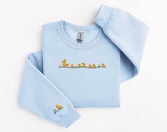 May include: A light blue sweatshirt with a line of yellow rubber ducklings embroidered on the front. The sweatshirt has a crew neck and long sleeves.