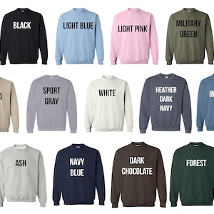 May include: A collection of crewneck sweatshirts in various colors, including black, light blue, light pink, military green, sand, sport gray, white, heather dark navy, indigo, ash, navy blue, dark chocolate, and forest. Each sweatshirt has the color name printed in white.
