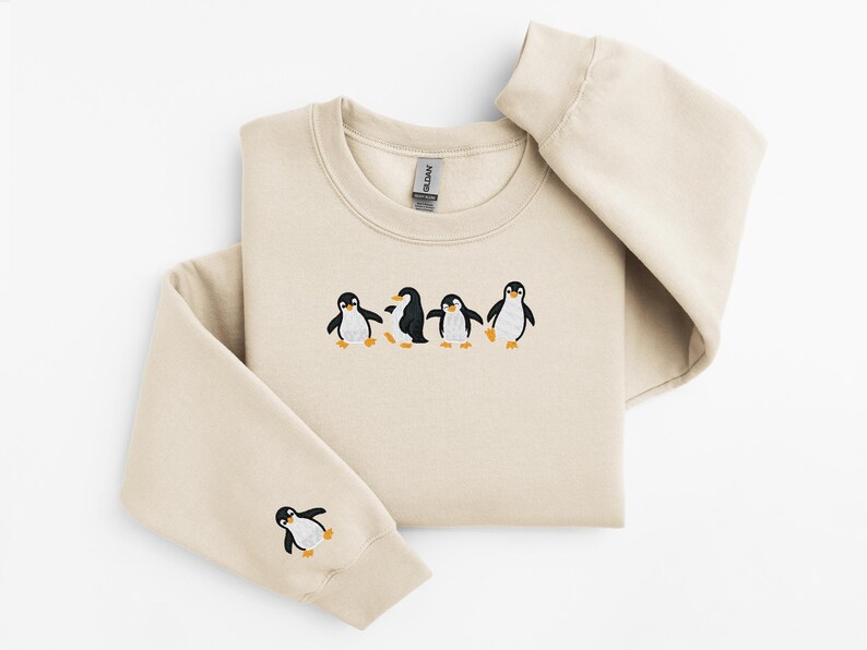 Pu&ograve; includere: Una felpa beige con girocollo e maniche lunghe. La parte anteriore della felpa presenta un disegno ricamato di quattro pinguini. Un pinguino &egrave; ricamato anche sulla manica sinistra.