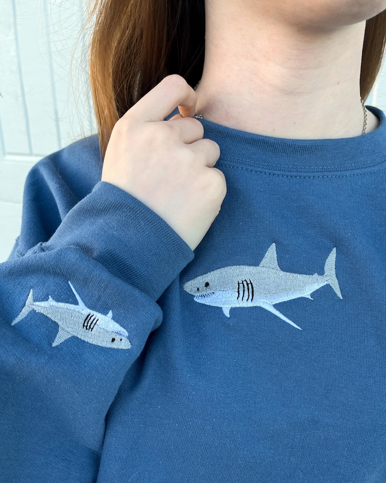 May include: A blue sweatshirt with a white embroidered shark on the front and a smaller white embroidered shark on the sleeve.
