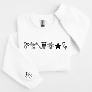 May include: White sweatshirt with black medical-themed graphics. The design includes a bow, knee joint, reflex hammer, medical symbol, star, and stethoscope. A medical symbol is also on the sleeve.