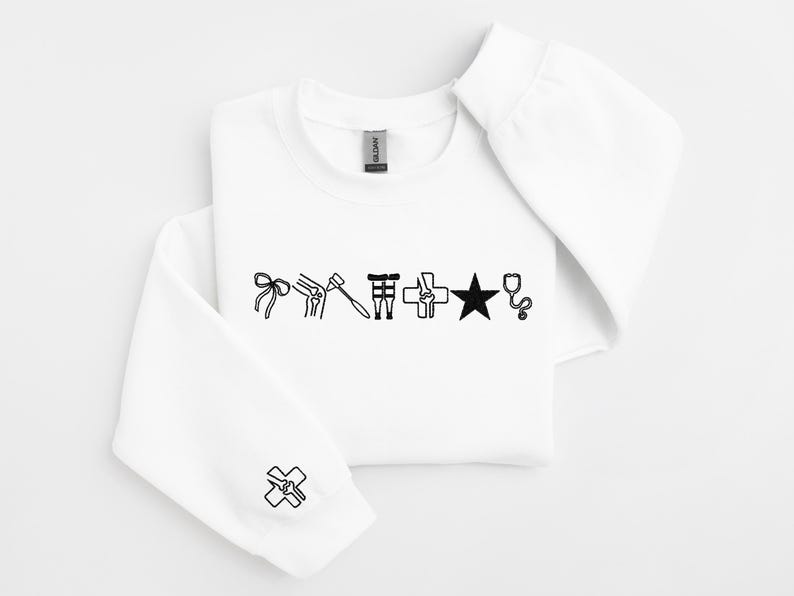 May include: White sweatshirt with black medical-themed graphics. The design includes a bow, knee joint, reflex hammer, medical symbol, star, and stethoscope. A medical symbol is also on the sleeve.