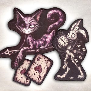 Könnte beinhalten: Ein Set aus vier bestickten Aufnähern mit einer lila grinsenden Katze mit langem Schwanz, einem weißen Kaninchen mit Taschenuhr und zwei Spielkarten mit dem Pik-Ass-Symbol. Die Motive sind in einem dunklen, detaillierten Illustrationsstil gehalten.
