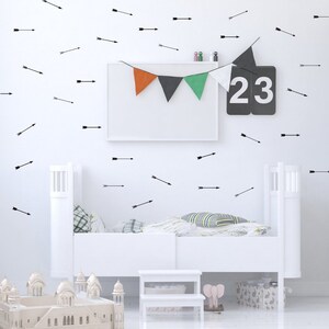 May include: A white crib with black arrow decals on the wall behind it. There are also colorful triangle flags hanging above the crib. The number 23 is displayed on a black sign.