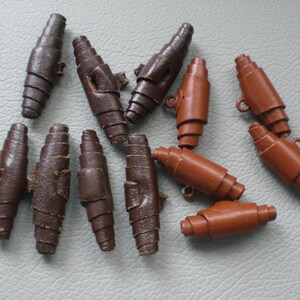May include: A collection of brown and orange leather toggles, some with metal rings. These toggles are used for fastening clothing or other items.