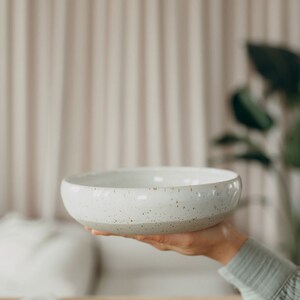 Peut inclure: Un bol en c&eacute;ramique blanche avec un gla&ccedil;age mouchet&eacute;. Le bol est tenu dans une main.