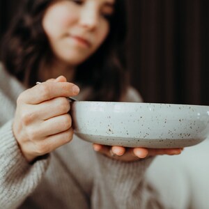 Peut inclure: Une personne tenant un bol en c&eacute;ramique gris clair avec un motif mouchet&eacute;. Le bol est vide.