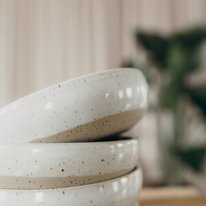 Peut inclure: Un ensemble de quatre bols en c&eacute;ramique blanche avec un gla&ccedil;age mouchet&eacute;. Les bols sont embo&icirc;t&eacute;s et ont un aspect rustique et artisanal.