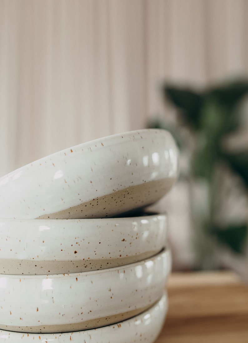 Peut inclure: Un ensemble de quatre bols en c&eacute;ramique blanche avec un gla&ccedil;age mouchet&eacute;. Les bols sont embo&icirc;t&eacute;s et ont un aspect rustique et artisanal.