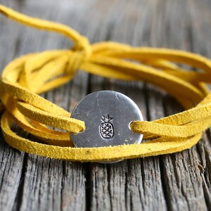 May include: A yellow leather wrap bracelet with a silver charm featuring a pineapple design.