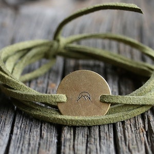 May include: A green leather wrap bracelet with a brass charm featuring a mountain silhouette.