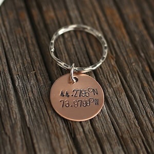 May include: A copper keychain with a silver ring. The keychain has the coordinates "44.2785°N 73.9799°W" engraved on it.