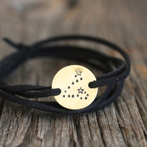 May include: A black leather wrap bracelet with a gold-toned circular charm featuring a constellation design.