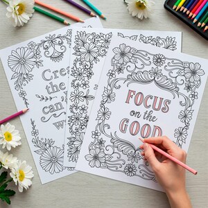 May include: Three black and white coloring pages with floral designs and inspirational quotes. The quotes are "Create the you can be", "Focus on the good", and "You are enough".