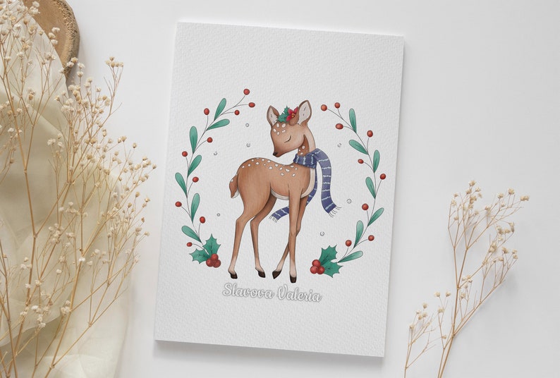 May include: A watercolor illustration of a fawn wearing a blue scarf and a holly wreath on its head. The fawn is standing in a wreath of green leaves and red berries. The text "Slavova Valeria" is written below the fawn.