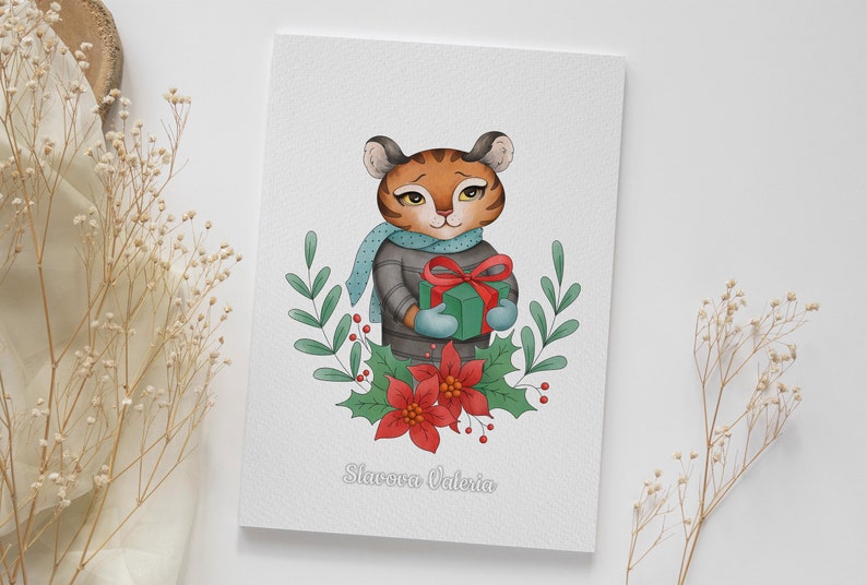 May include: A Christmas card featuring a cartoon tiger wearing a blue scarf and a grey sweater, holding a green gift box with a red bow. The tiger is surrounded by green leaves, red berries, and a red poinsettia flower. The card reads "Slavaova Valeria".