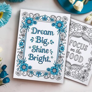 May include: Two printable coloring pages with inspirational quotes. The first page features a floral border with blue flowers and the quote "Dream Big, Shine Bright." The second page features a black and white floral border with the quote "Focus on the Good."