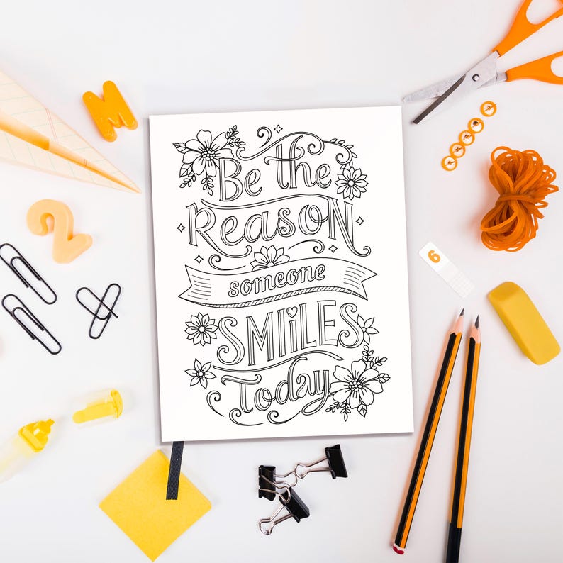 May include: A black and white printable coloring page with the text "Be the reason someone smiles today" surrounded by flowers. The page is on a white surface with various office supplies, including pencils, a rubber eraser, paper clips, and a pair of scissors.