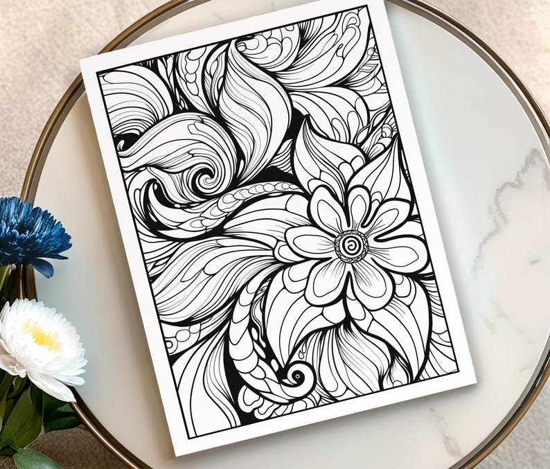 May include: A black and white floral line art print featuring a large flower and swirling leaf-like patterns. The artwork is on a white paper, resting on a marble-like surface. The print is suitable for coloring or as a decorative piece.