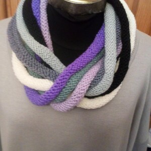 Pu&ograve; includere: Una sciarpa infinita di maglia multicolore con sfumature di viola, bianco, grigio e nero.