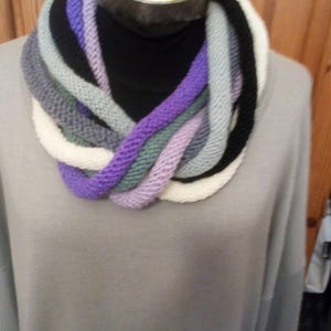 Pu&ograve; includere: Una sciarpa infinita di maglia multicolore con sfumature di viola, bianco, grigio e nero. La sciarpa &egrave; esposta su un manichino.