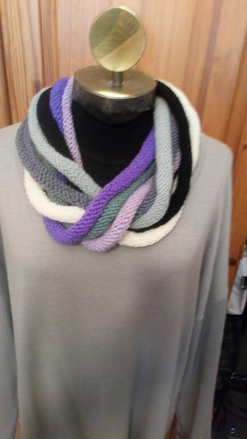 Pu&ograve; includere: Una sciarpa infinita di maglia multicolore con sfumature di viola, bianco, grigio e nero. La sciarpa &egrave; esposta su un manichino.