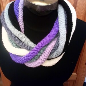 Pu&ograve; includere: Una sciarpa infinita a maglia multicolore con strisce viola, bianche, grigie e nere.
