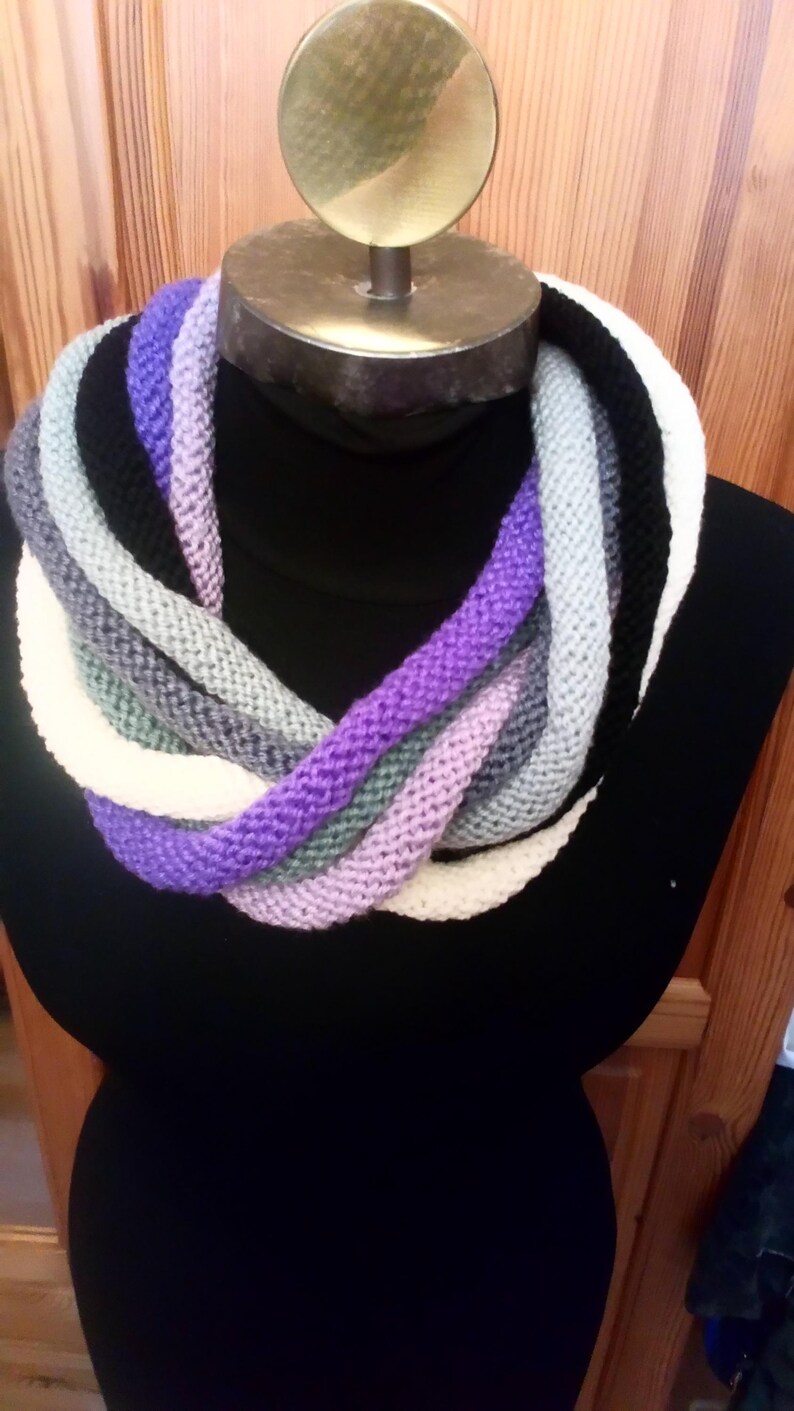 Pu&ograve; includere: Una sciarpa infinita a maglia multicolore con strisce viola, bianche, grigie e nere.