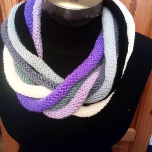 Pu&ograve; includere: Una sciarpa infinita a maglia multicolore con strisce viola, bianche, grigie e nere.