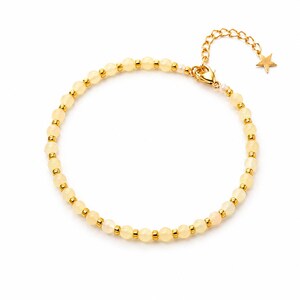 Peut inclure: Un bracelet délicat composé de petites perles jaune pâle entrecoupées d'accents dorés. Le bracelet est doté d'une chaîne dorée avec un charm en forme d'étoile à l'extrémité. Le fermoir est également doré.