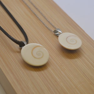 Peut inclure: Deux colliers avec des pendentifs en coquillage. Les colliers sont sur une surface en bois. L'un a un cordon noir et l'autre une chaîne argentée.