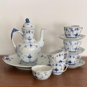 Peut inclure: Un service à thé en porcelaine blanche orné d'un délicat motif floral bleu. L'ensemble comprend une théière avec couvercle sur un plateau ovale assorti, quatre tasses avec soucoupes et un petit bol. Chaque pièce présente des motifs de fleurs.