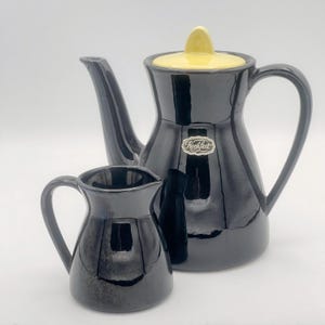 Op de afbeelding: Een zwarte keramische theepot en roomkan set met een geel deksel. De theepot heeft een zilveren label met de tekst "Kochfest".