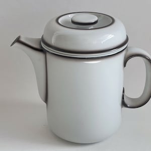 Op de afbeelding: Witte koffiekan van keramiek met een zwart deksel en handvat. De kan heeft een zwarte streep rond de boven- en onderkant.