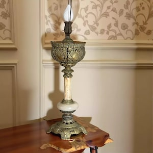 May include: An antique brass table lamp with an ornate, filigree shade and a marble column base. The lamp features a clear glass globe and sits on a decorative, openwork base. The lamp is a vintage piece, showcasing intricate details and a classic design.