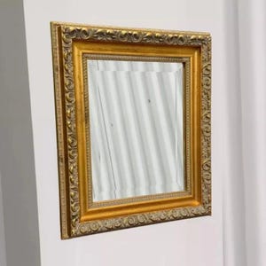 May include: A rectangular wall mirror featuring a thick, ornate gold frame with intricate embossed scrollwork and floral patterns. The reflective glass surface is clear and smooth, set within a deep, multi-layered border that adds depth.