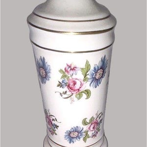 May include: A white ceramic lamp base with a floral pattern of pink roses and blue daisies, accented by gold horizontal bands. A yellow Stanley measuring tape is placed at the base, showing a width measurement of approximately 5 inches.