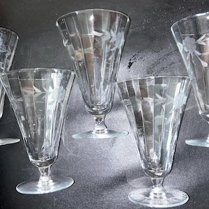 May include: Set of five clear glass goblets with etched floral designs. The goblets have a tall, slender shape with a wide bowl and a delicate stem.